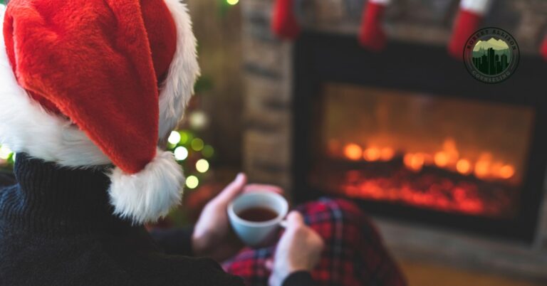 Sad man in santa hat drinking coffee and staring at fireplace